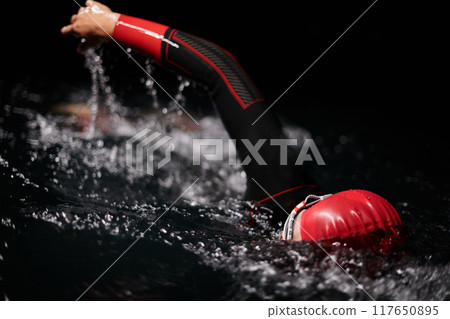 A determined professional triathlete undergoes rigorous night time training in cold waters, showcasing dedication and resilience in preparation for an upcoming triathlon swim competition 117650895