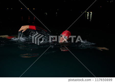 A determined professional triathlete undergoes rigorous night time training in cold waters, showcasing dedication and resilience in preparation for an upcoming triathlon swim competition 117650899