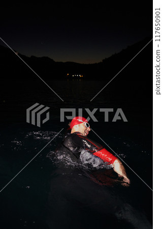 A determined professional triathlete undergoes rigorous night time training in cold waters, showcasing dedication and resilience in preparation for an upcoming triathlon swim competition 117650901