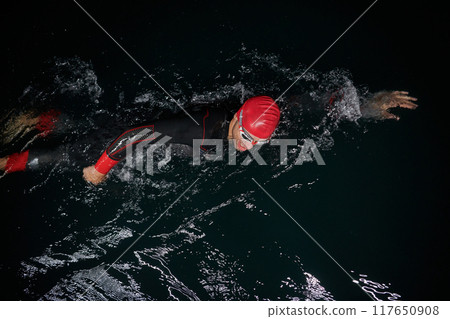 A determined professional triathlete undergoes rigorous night time training in cold waters, showcasing dedication and resilience in preparation for an upcoming triathlon swim competition 117650908