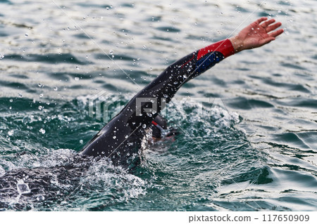 A professional triathlete trains with unwavering dedication for an upcoming competition at a lake, emanating a sense of athleticism and profound commitment to excellence. A professional triathlete trains with unwavering dedication for an upcoming competition at a lake, emanating a sense of athleticism and profound commitment to excellence. 117650909