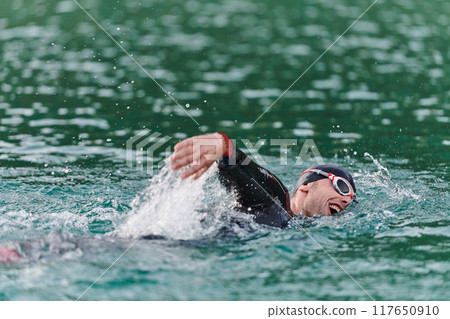 A professional triathlete trains with unwavering dedication for an upcoming competition at a lake, emanating a sense of athleticism and profound commitment to excellence. 117650910