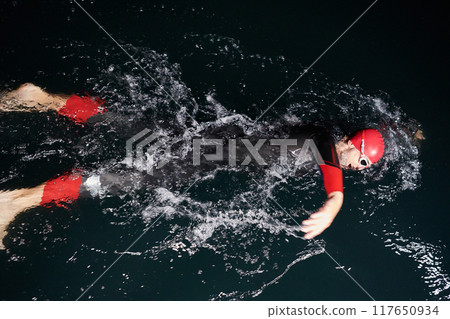 A determined professional triathlete undergoes rigorous night time training in cold waters, showcasing dedication and resilience in preparation for an upcoming triathlon swim competition 117650934