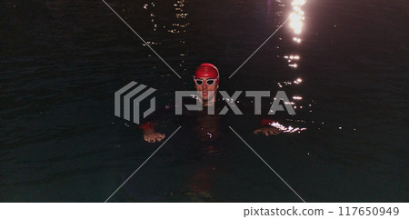 A determined professional triathlete undergoes rigorous night time training in cold waters, showcasing dedication and resilience in preparation for an upcoming triathlon swim competition 117650949