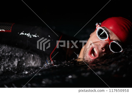 A determined professional triathlete undergoes rigorous night time training in cold waters, showcasing dedication and resilience in preparation for an upcoming triathlon swim competition A determined professional triathlete undergoes rigorous night time training in cold waters, showcasing dedication and resilience in preparation for an upcoming triathlon swim competition 117650958