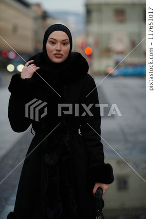 Muslim woman walking on an urban city street on a cold winter night wearing hijab Muslim woman walking on an urban city street on a cold winter night wearing hijab 117651017
