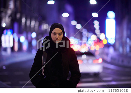 Muslim woman walking on an urban city street on a cold winter night wearing hijab 117651018