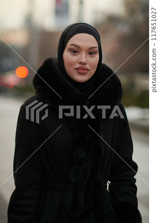Muslim woman walking on an urban city street on a cold winter night wearing hijab 117651027