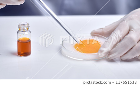 Close up shot in scene of scientist conducts a chemical experiment in laboratory, carefully stir white cream and yellow essence in petri dish. Cosmetic advertising photo with space for designing Close up shot in scene of scientist conducts a chemical experiment in laboratory, carefully stir white cream and yellow essence in petri dish. Cosmetic advertising photo with space for designing 117651538