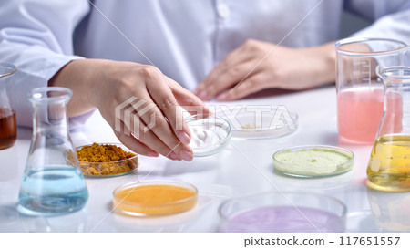 Cosmetic advertising template photo with laboratory concept was shot from close up side view, scientist lift a glass petri dish contains white cream up, several lab glassware scattered lay on table Cosmetic advertising template photo with laboratory concept was shot from close up side view, scientist lift a glass petri dish contains white cream up, several lab glassware scattered lay on table 117651557