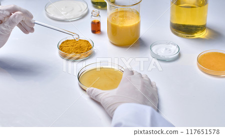 Template photo for cosmetic advertising, which extracted from natural ingredients like turmeric. Cosmetic research in laboratory from high angle shot with plenty lab glassware placed on white table 117651578