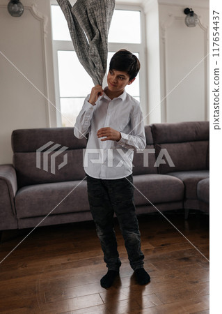 A young boy playfully holding up jacket in a cozy living room during daylight hours A young boy playfully holding up jacket in a cozy living room during daylight hours 117654437