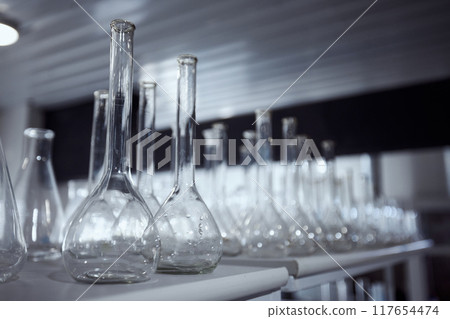 Row of various glass beakers and flasks, arranged on a laboratory bench in a dimly lit room. Foundation for a perfect brew. 117654474