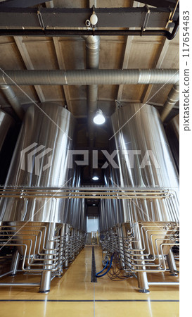 Large, modern brewery with several stainless steel fermentation tanks and pipes, connected by a network of pipes and valves. Large, modern brewery with several stainless steel fermentation tanks and pipes, connected by a network of pipes and valves. 117654483