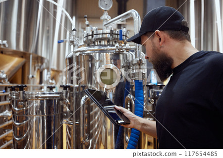 Concentrated man, technologist examining brewing equipment, maintaining thigh standards necessary for quality beer production. 117654485