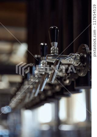 Close-up of row of shiny chrome beer taps with black handles, mounted on dark background. Modern beer brewing company 117654519