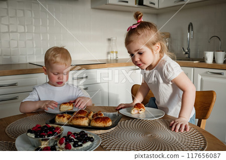 Children enjoying breakfast together in a modern kitchen while sharing delicious pastries and fruits Children enjoying breakfast together in a modern kitchen while sharing delicious pastries and fruits 117656087