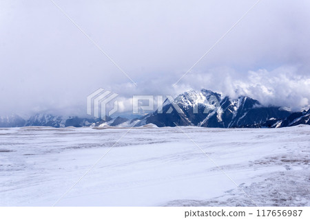 landscape of glacial highland plateau, view from the surface of the glacier, mountains in the clouds are visible in the distance landscape of glacial highland plateau, view from the surface of the glacier, mountains in the clouds are visible in the distance 117656987