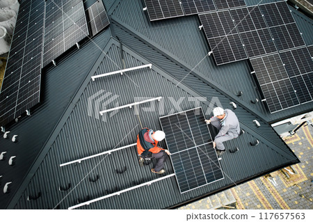 Installers building photovoltaic solar module station on roof of house. Men electricians in helmets installing solar panel system outdoors. Concept of alternative and renewable energy. Aerial view. 117657563