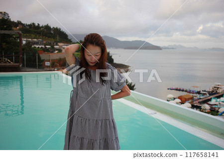 Dolsan-eup, Yeosu-si, South Korea - July 26, 2024: Young woman watching sunrise at a resort with a swimming pool overlooking the sea in Yeosu 117658141