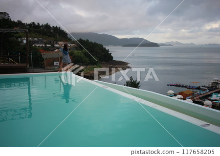 Dolsan-eup, Yeosu-si, South Korea - July 26, 2024: Young woman watching sunrise at a resort with a swimming pool overlooking the sea in Yeosu 117658205