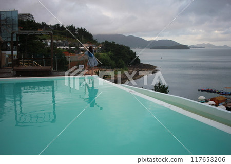 Dolsan-eup, Yeosu-si, South Korea - July 26, 2024: Young woman watching sunrise at a resort with a swimming pool overlooking the sea in Yeosu 117658206