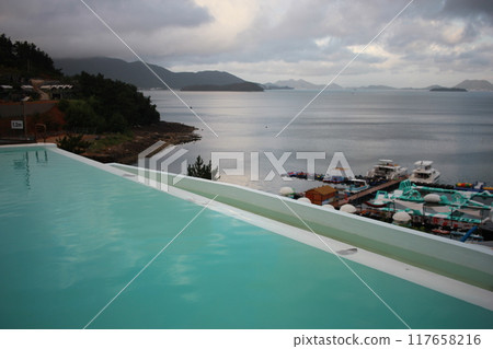 Dolsan-eup, Yeosu-si, South Korea - July 26, 2024: Young woman watching sunrise at a resort with a swimming pool overlooking the sea in Yeosu Dolsan-eup, Yeosu-si, South Korea - July 26, 2024: Young woman watching sunrise at a resort with a swimming pool overlooking the sea in Yeosu 117658216