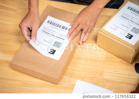Close up hands of an online seller man putting shipping label on the product box before sending it off to his customer 117658322