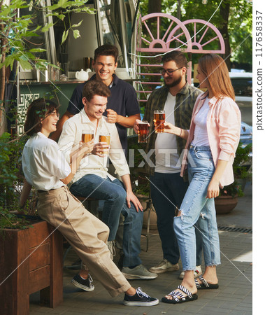 Warm sunny day and relaxing vibes with friends, Happy, smiling young people, men and women meeting at outdoor bar, restaurant and enjoying beer Warm sunny day and relaxing vibes with friends, Happy, smiling young people, men and women meeting at outdoor bar, restaurant and enjoying beer 117658337