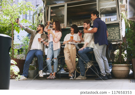 Happy smiling people, friends, men and women meeting at local outdoor bar, drinking beer and taking selfie with mobile phone. Cozy memories 117658353