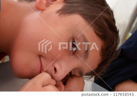 A relaxed child look in camera while he rests his head on one arm. 117658543