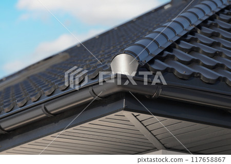Close-up house roof with steel roofing sheet. Black modular tile effect roof panel. Traditional metal shingle tiles. Profiled metallic corrugated pantile as clay or concrete slate. Building's covering 117658867