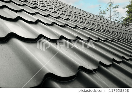 Close-up house roof with steel roofing sheet. Gray modular tile effect roof panel. Traditional metal shingle tiles. Profiled metallic corrugated pantile as clay or concrete slate. Building's covering Close-up house roof with steel roofing sheet. Gray modular tile effect roof panel. Traditional metal shingle tiles. Profiled metallic corrugated pantile as clay or concrete slate. Building's covering 117658868