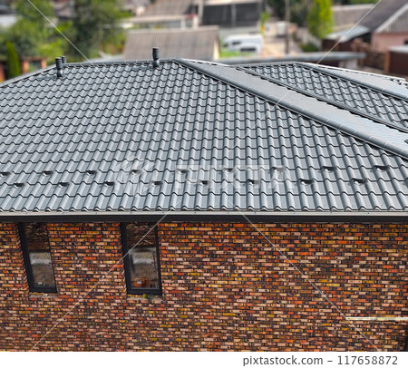 Close-up house roof with steel roofing sheet. Gray modular tile effect roof panel. Traditional metal shingle tiles. Profiled metallic corrugated pantile as clay or concrete slate. Building's covering Close-up house roof with steel roofing sheet. Gray modular tile effect roof panel. Traditional metal shingle tiles. Profiled metallic corrugated pantile as clay or concrete slate. Building's covering 117658872