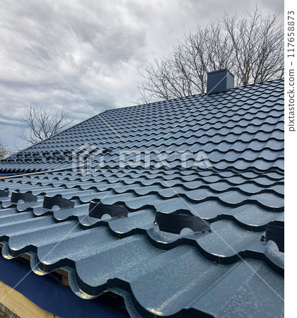 Close-up house roof with steel roofing sheet. Blue modular tile effect roof panel. Traditional metal shingle tiles. Profiled metallic corrugated pantile as clay or concrete slate. Building's covering Close-up house roof with steel roofing sheet. Blue modular tile effect roof panel. Traditional metal shingle tiles. Profiled metallic corrugated pantile as clay or concrete slate. Building's covering 117658873