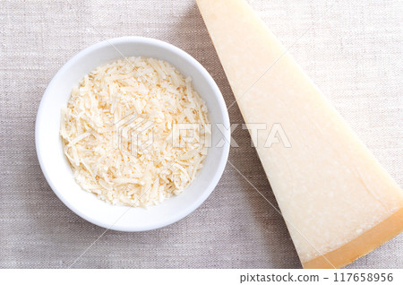 Grated parmesan cheese, Parmigiano Reggiano in a wooden bowl on linen, with whole piece of cheese on the right side. Italian hard, granular cheese, produced from cow's milk, aged at least 12 months. 117658956