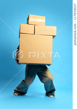 Balancing towering stack of boxes, only person's legs visible against blue studio background. Concept of Black Friday sale. 117659037