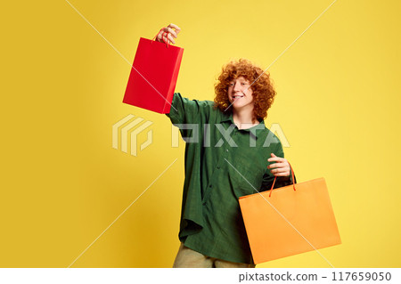 Happy, stylish young man holding colorful bag with copy space to insert your text against yellow background. Concept of Black Friday 117659050
