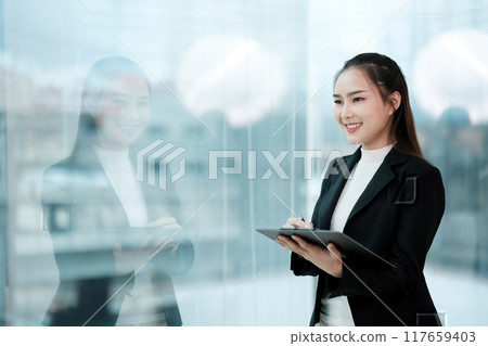 A woman in a business suit is smiling and holding a tablet 117659403