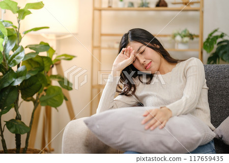 A woman is sitting on a couch with a pillow on her lap A woman is sitting on a couch with a pillow on her lap 117659435