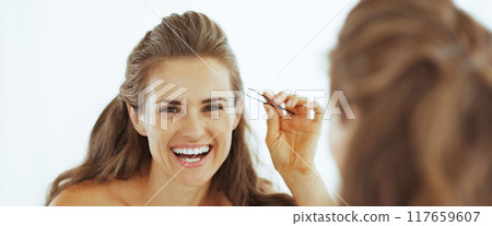 Happy young woman with tweezers in bathroom 117659607