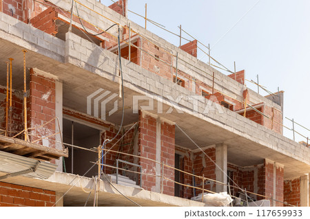 Close-up of an urban construction site with unfinished brick and concrete building under clear skies. Perfect for content related to urban development, architecture, and construction. 117659933