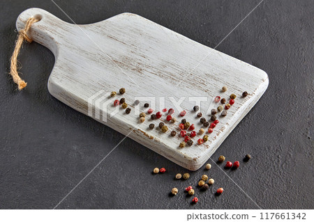 White wooden cutting board with scattered colorful peppercorns on a black stone table 117661342