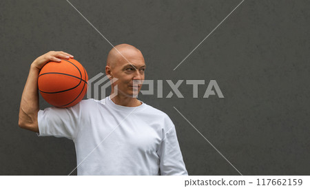 Banner of handsome sporty adult man in white t-shirt holding basketball orange ball on shoulder near the dark wall. Copy space. Banner of handsome sporty adult man in white t-shirt holding basketball orange ball on shoulder near the dark wall. Copy space. 117662159