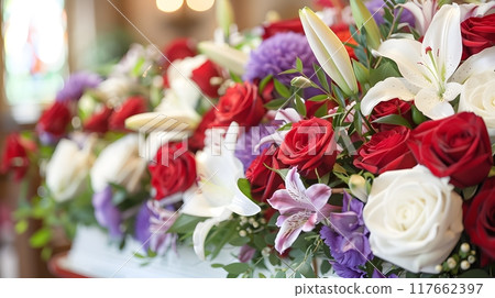 A lovely dark wood coffin adorned with roses, lilies, and carnations creates a lush display. Shot up close, the image captures intricate details, enhanced by soft, diffused light for a warm atmosphere A lovely dark wood coffin adorned with roses, lilies, and carnations creates a lush display. Shot up close, the image captures intricate details, enhanced by soft, diffused light for a warm atmosphere 117662397
