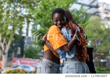 Joyful cheerful African American women hugging with love, happily smiling laughing outside at street 117663807