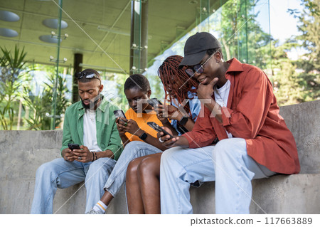Phone addiction. Group of black focused student friends stare at smartphone screens more than once. 117663889