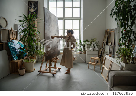 Serious focused female artist creating huge impressive oil painting. Painstaking working process. 117663959