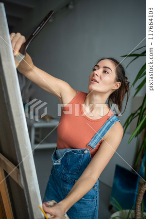 Confident proud female artist painting picture in light art studio workshop. Creative process. 117664103