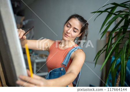 Confident proud female artist painting picture in light art studio workshop. Creative process. 117664144